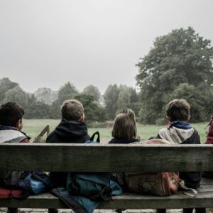 five children sitting on bench front of trees